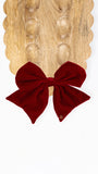 A deep burgundy velvet bow displayed on a scalloped wooden board against a clean white background.