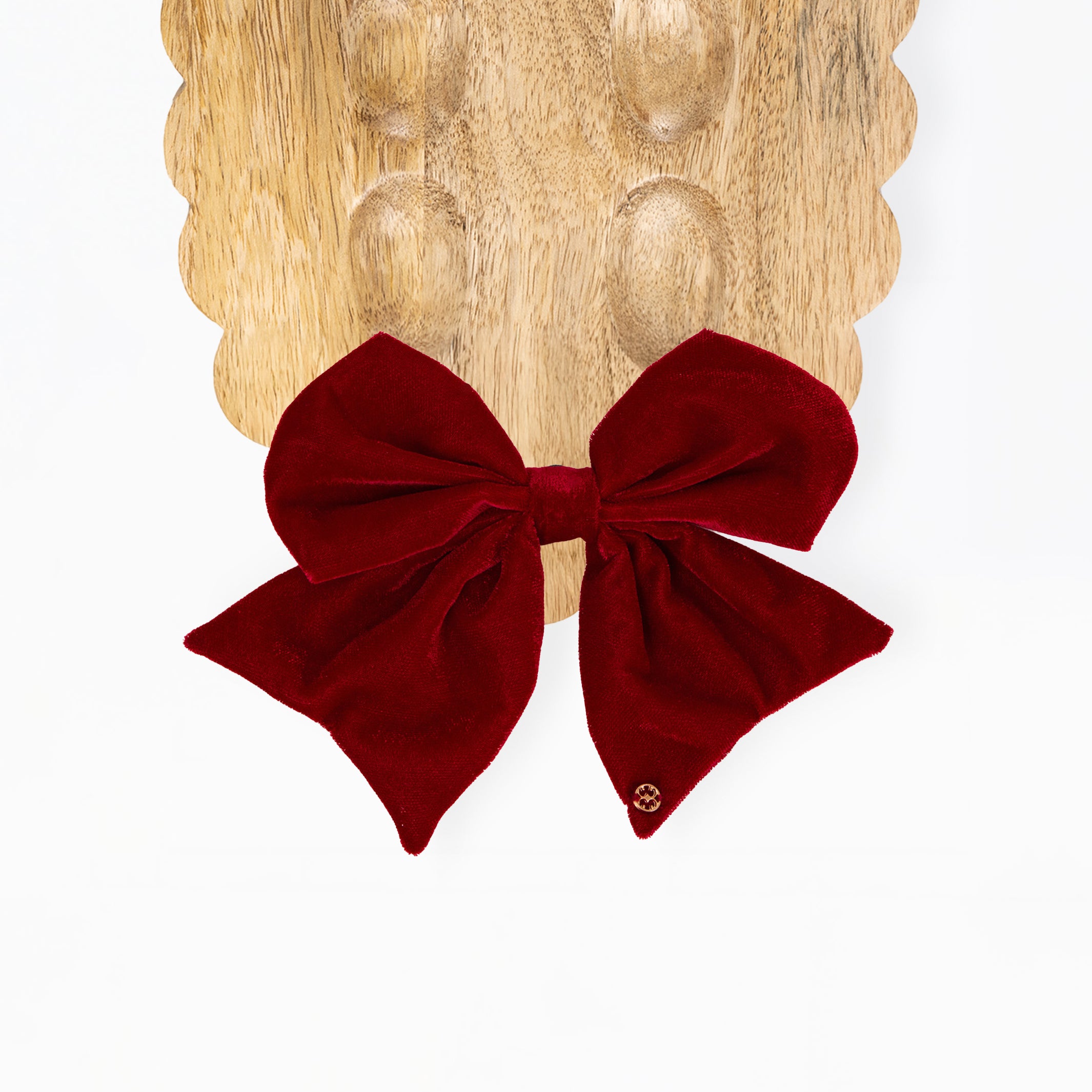 A deep burgundy velvet bow displayed on a scalloped wooden board against a clean white background.