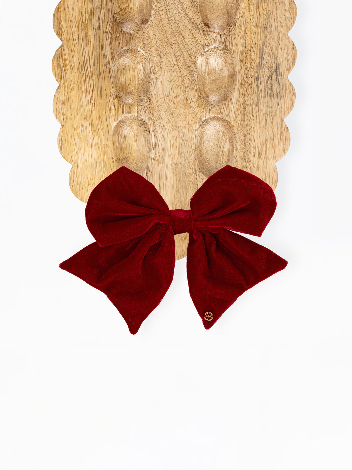 A deep burgundy velvet bow displayed on a scalloped wooden board against a clean white background.