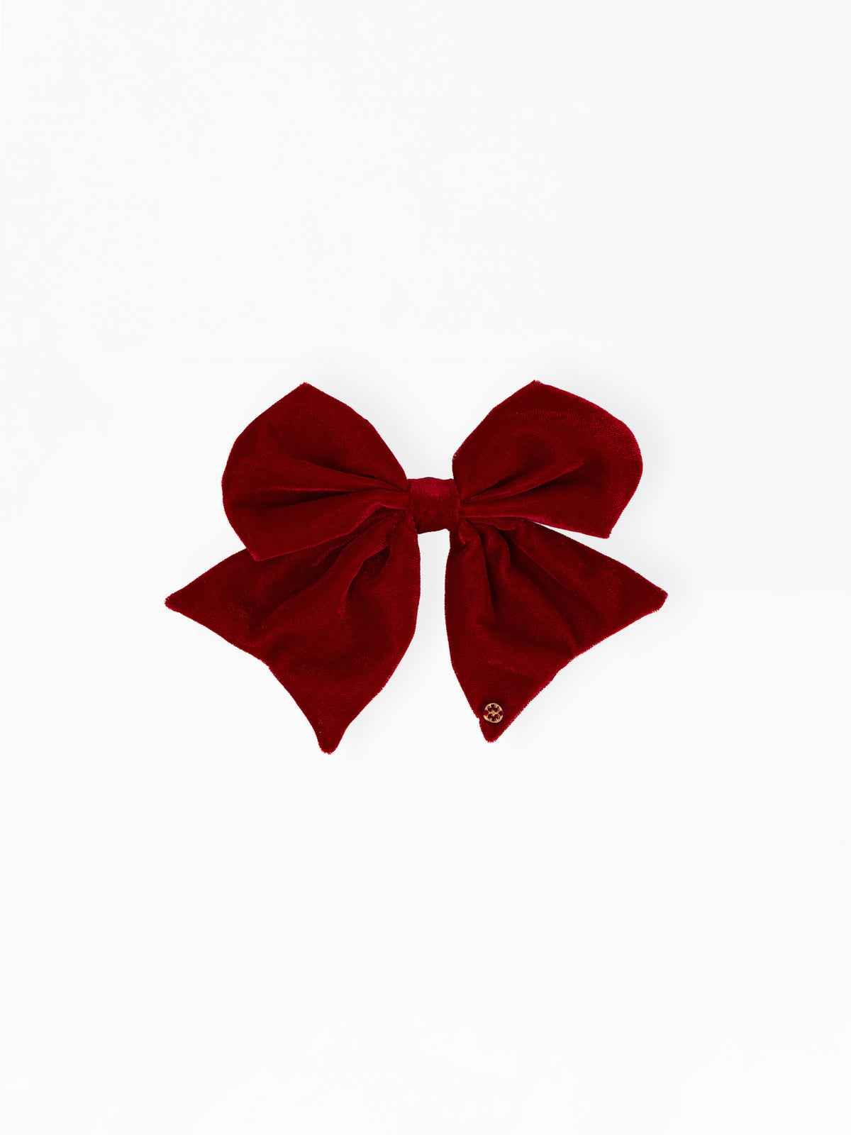 A large deep red velvet bow with a small gold logo charm on one tip, displayed flat against a solid white background.