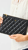 Person holding a black quilted clutch bag against a neutral background