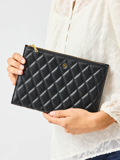 Person holding a black quilted clutch bag against a neutral background