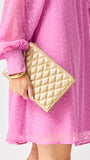 Person wearing a pink dress holding a gold quilted clutch against a white background