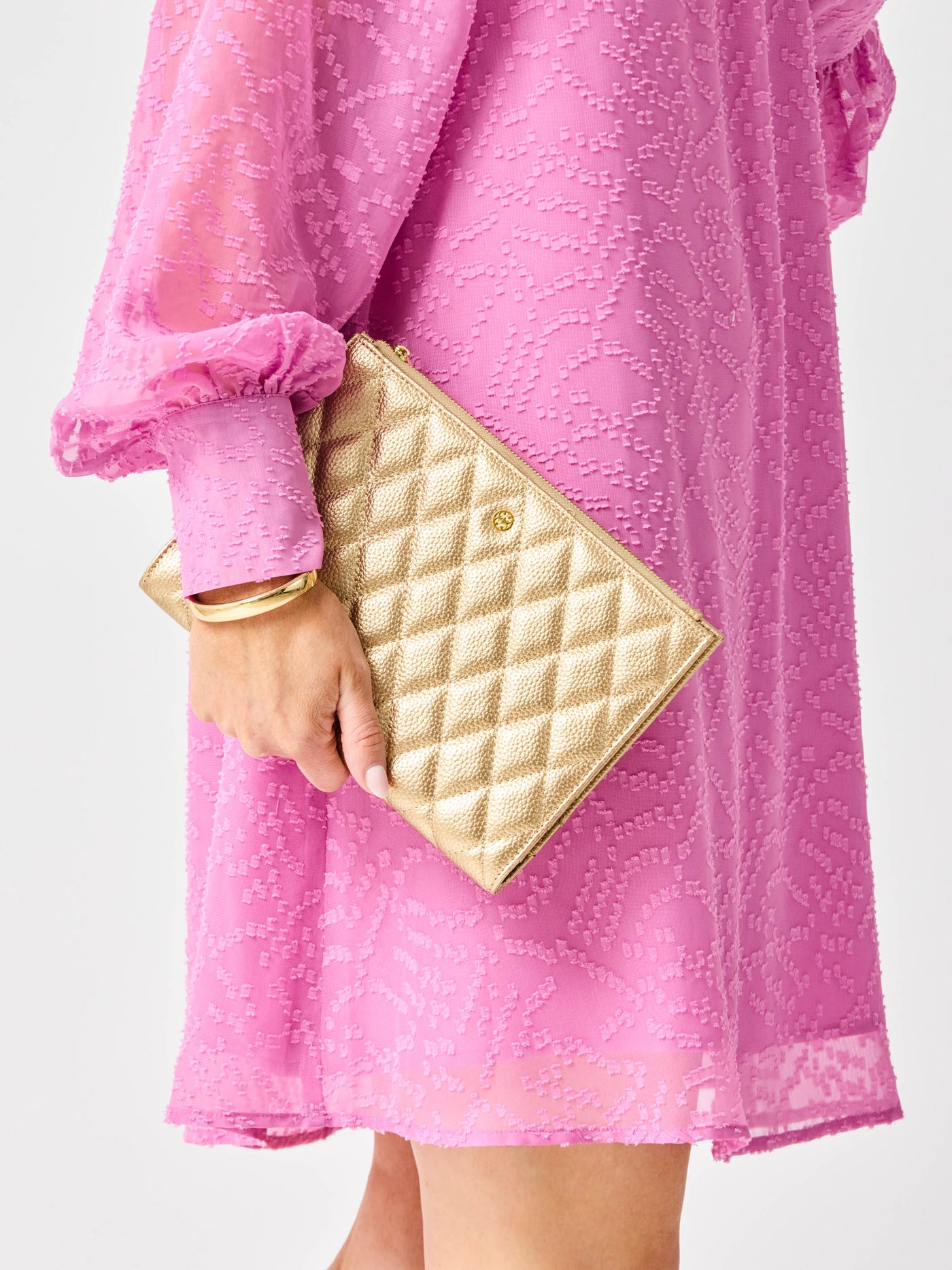 Person wearing a pink dress holding a gold quilted clutch against a white background
