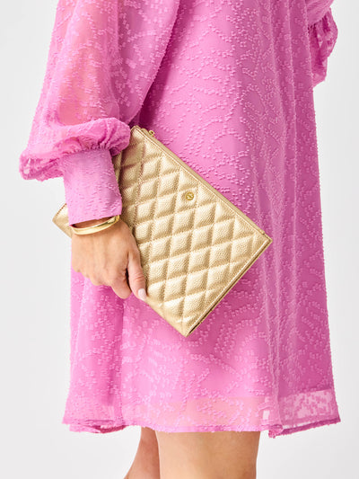 Person wearing a pink dress holding a gold quilted clutch against a white background