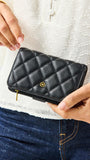 Person holding a black quilted wallet with a brand logo against a white background