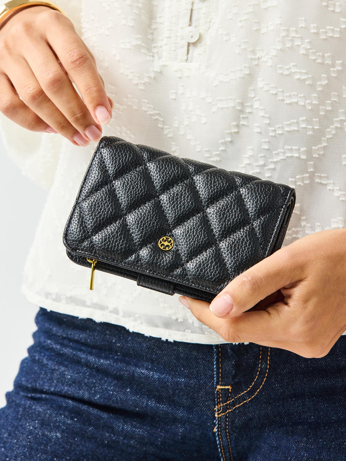 Person holding a black quilted wallet with a brand logo against a white background