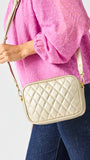 Person wearing a pink textured top and blue jeans holding a beige quilted handbag against a white background