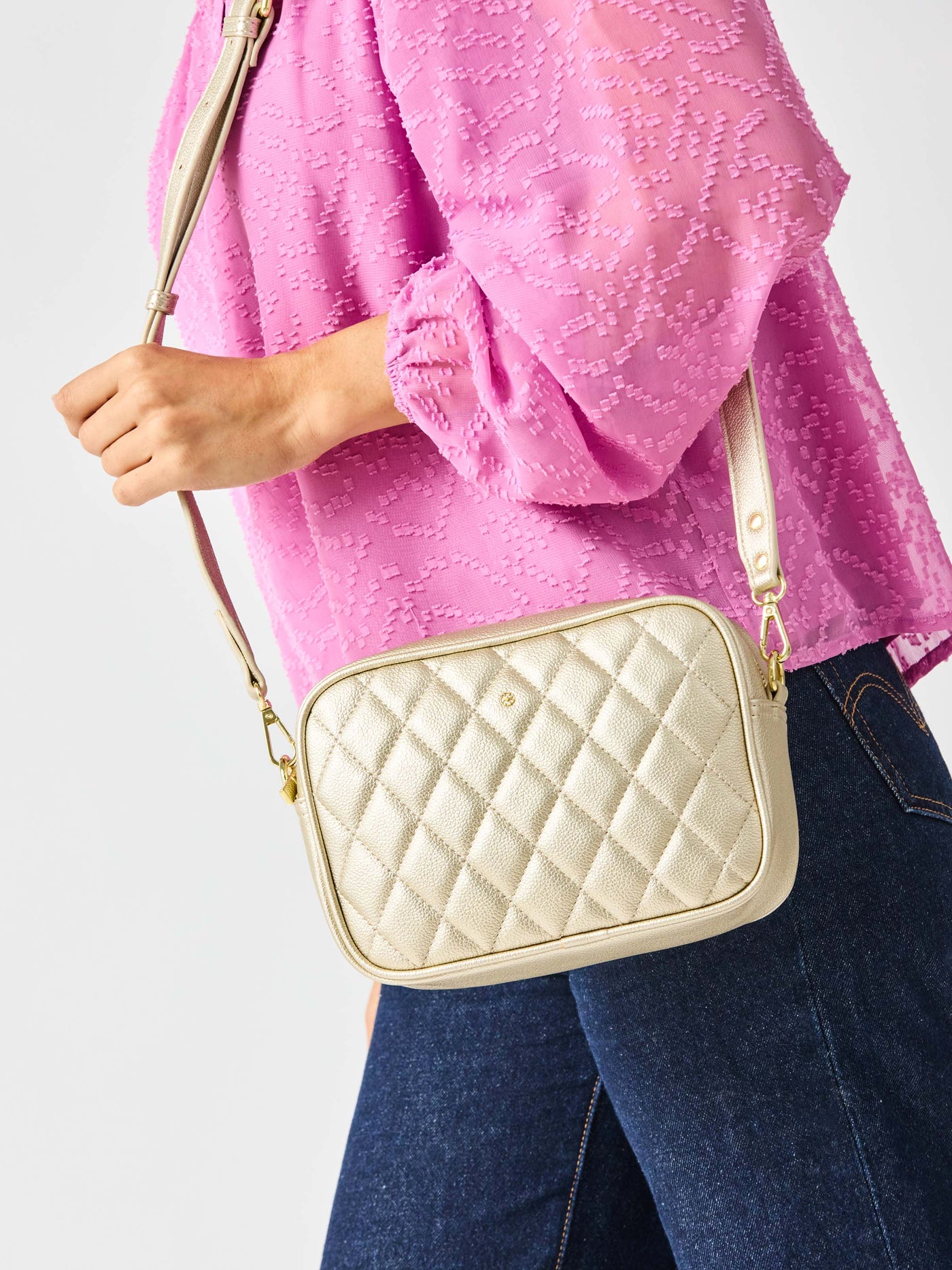 Person wearing a pink textured top and blue jeans holding a beige quilted handbag against a white background