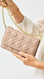 Beige quilted handbag with gold chain strap held by a person wearing a white sweater.