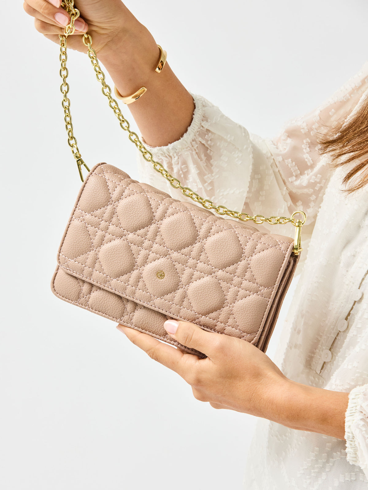 Beige quilted handbag with gold chain strap held by a person wearing a white sweater.