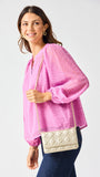 Woman wearing a pink blouse with a gold quilted handbag on a white background