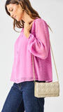 Woman wearing a pink blouse and blue jeans, holding a beige quilted handbag against a white background