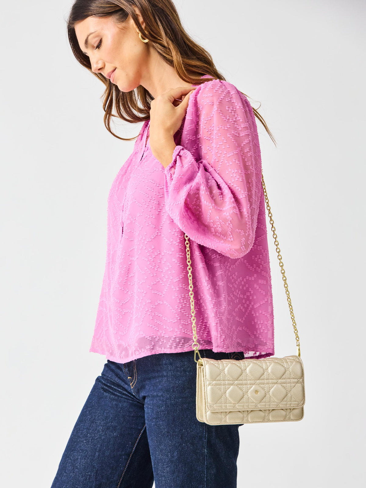 Woman wearing a pink blouse and blue jeans, holding a beige quilted handbag against a white background