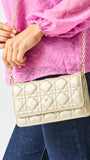 Person holding a gold quilted handbag with a pink top and blue jeans.