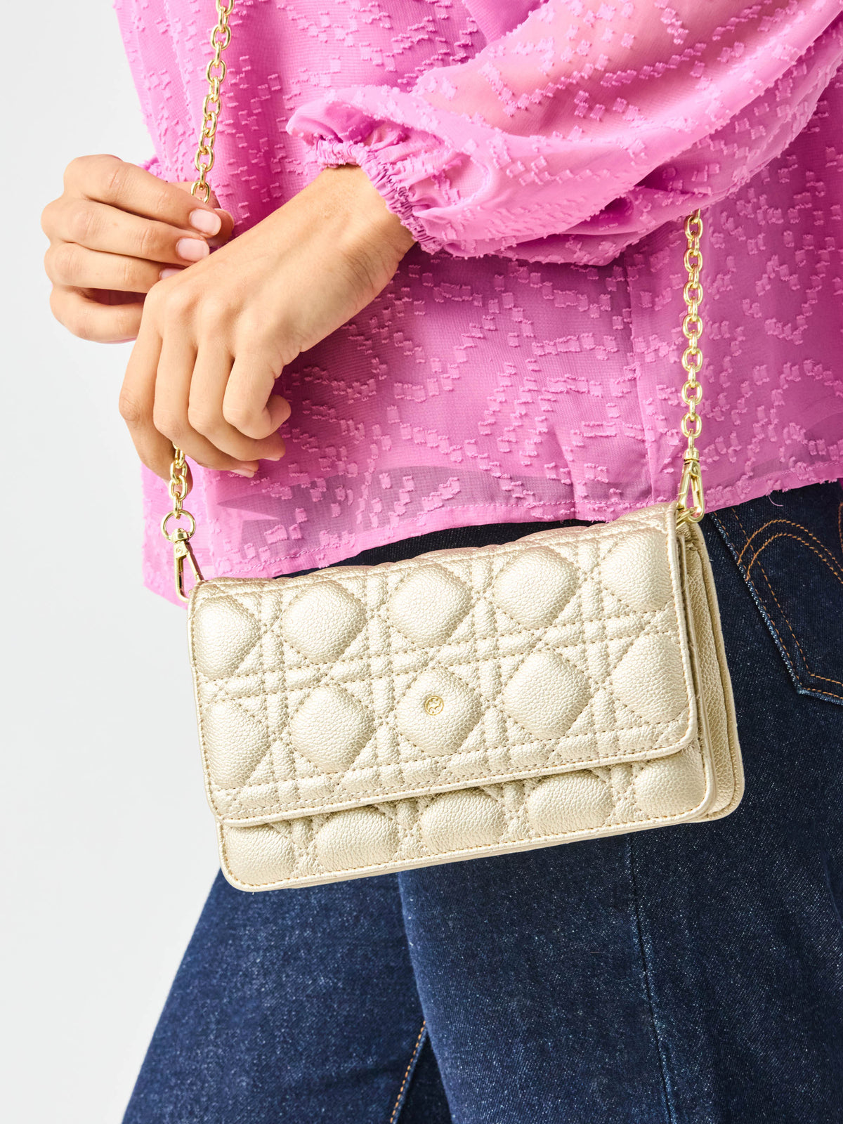 Person holding a gold quilted handbag with a pink top and blue jeans.