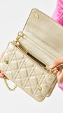 Champagne quilted handbag with gold chain strap held by a person wearing a pink top.