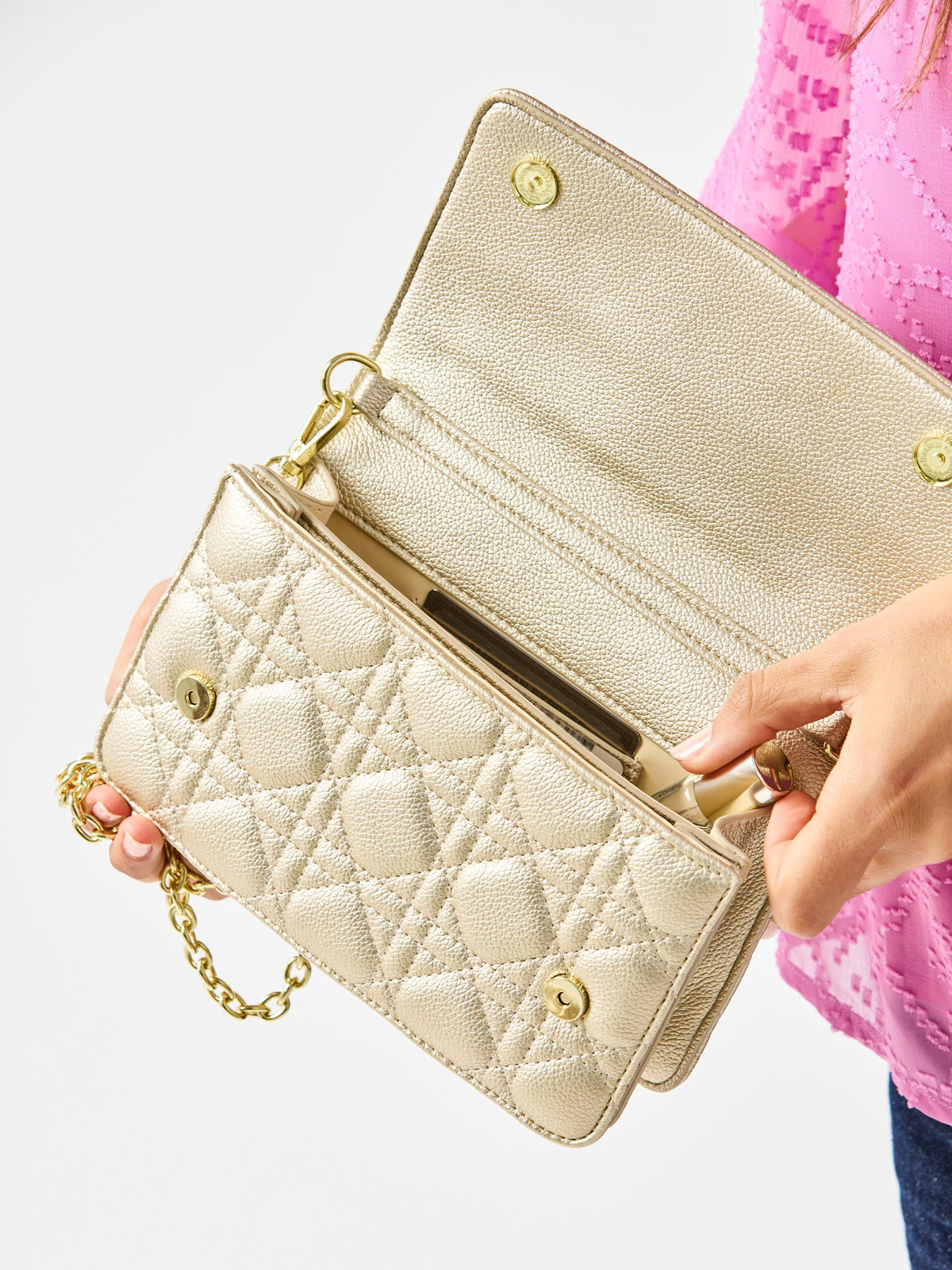 Champagne quilted handbag with gold chain strap held by a person wearing a pink top.