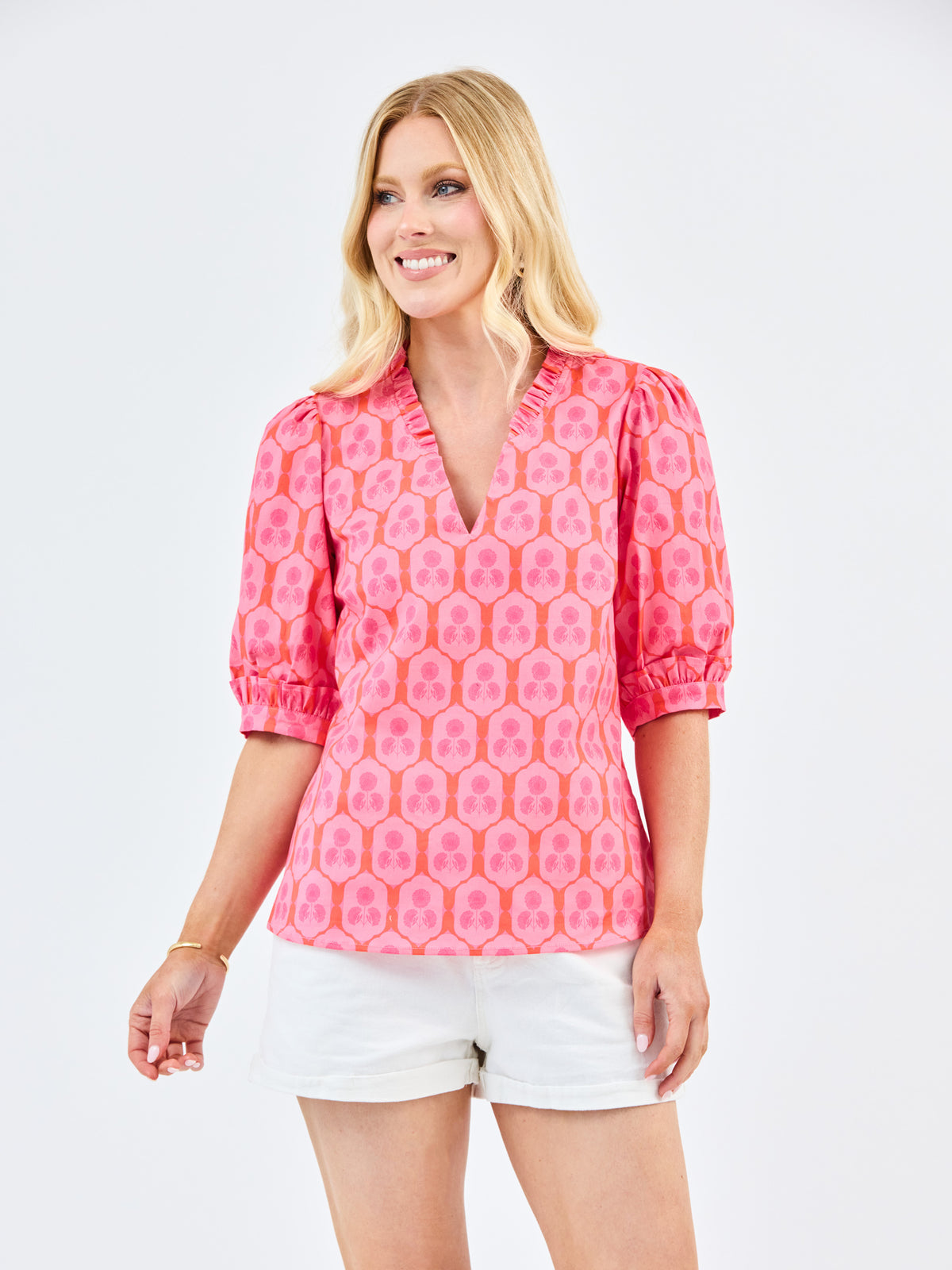 Woman wearing a pink patterned blouse and white shorts on a light gray background