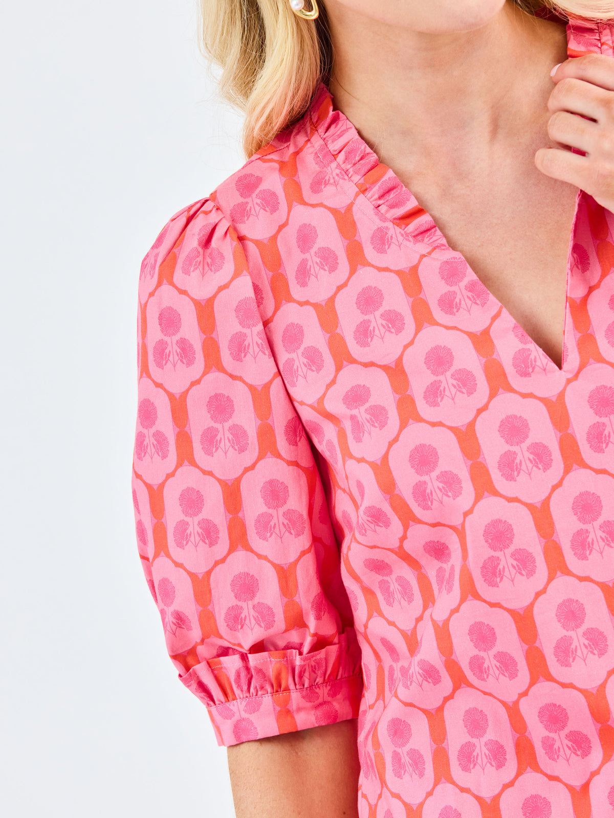 Close-up of a person wearing a pink and orange patterned blouse with a plain background