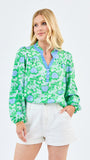Woman wearing a green floral blouse and white shorts on a light gray background