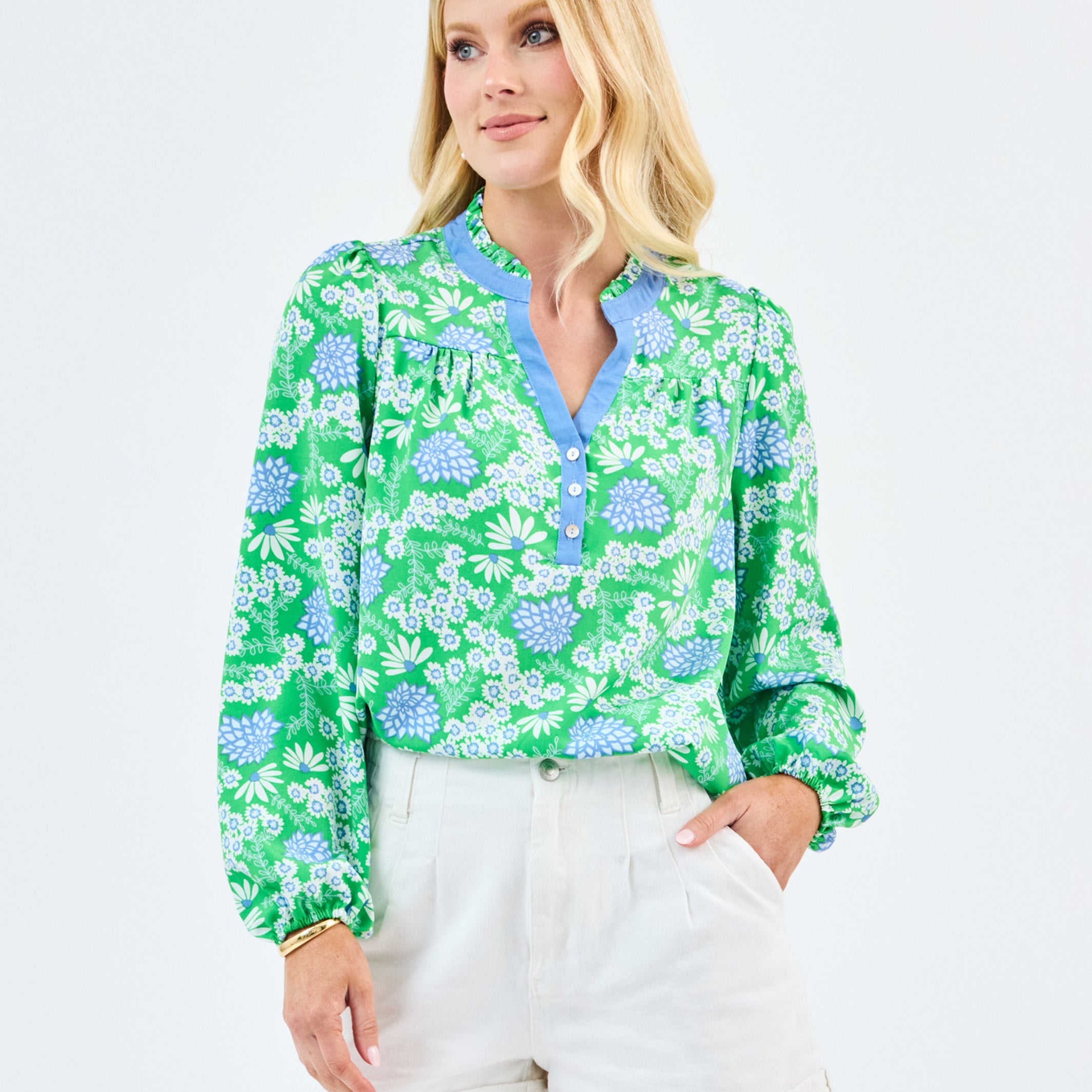Woman wearing a green floral blouse and white shorts on a light gray background