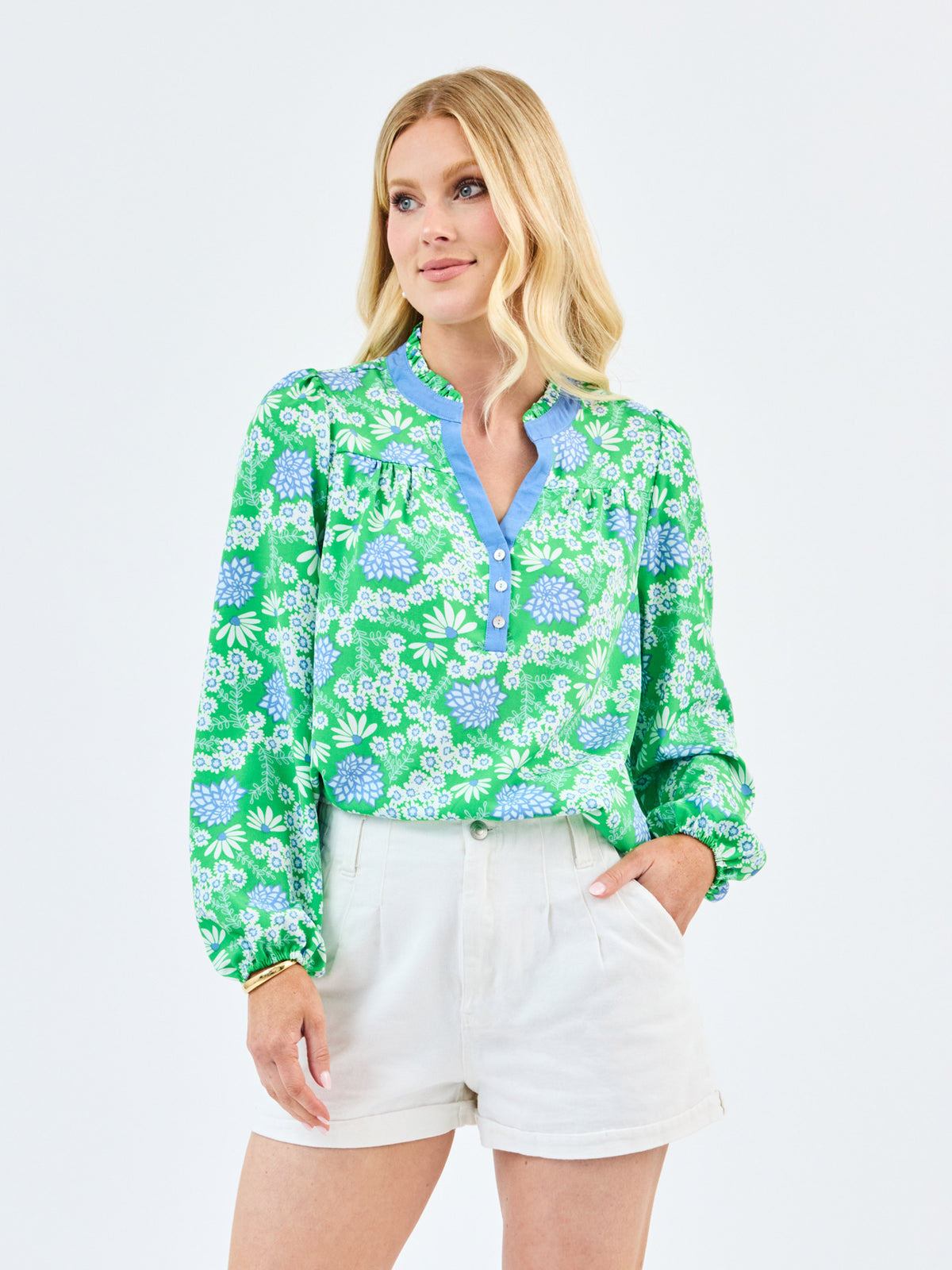 Woman wearing a green floral blouse and white shorts on a light gray background
