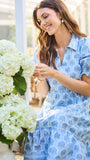 Woman in a blue floral dress holding white hydrangeas indoors.