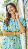Woman wearing a light blue dress with green leaf pattern standing outdoors.