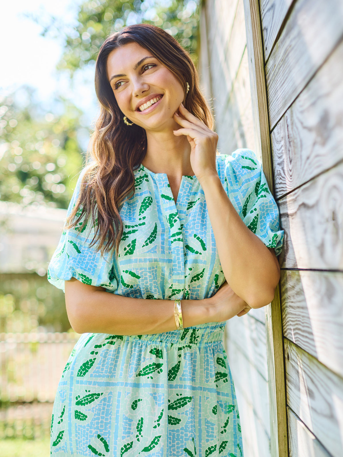 Woman wearing a light blue dress with green leaf pattern standing outdoors.