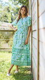 Woman in a green dress standing outdoors near a wooden wall.
