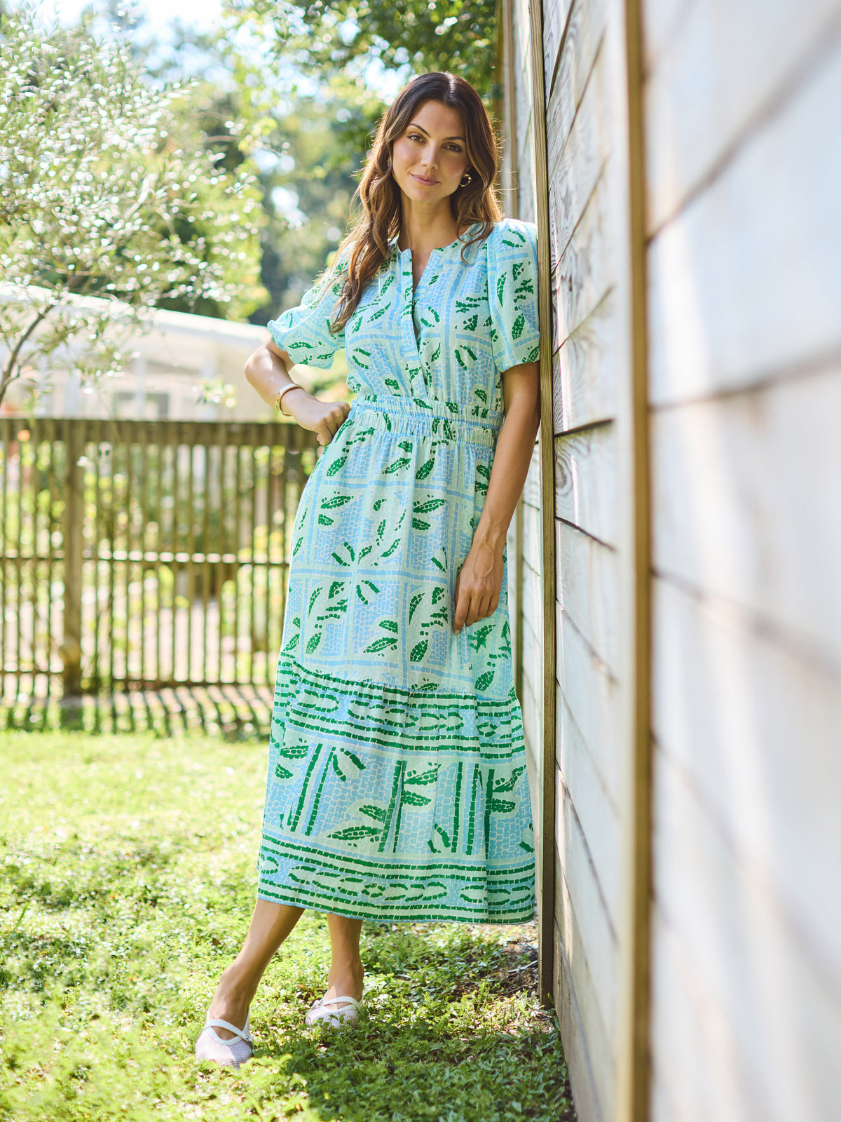 Woman in a green dress standing outdoors near a wooden wall.