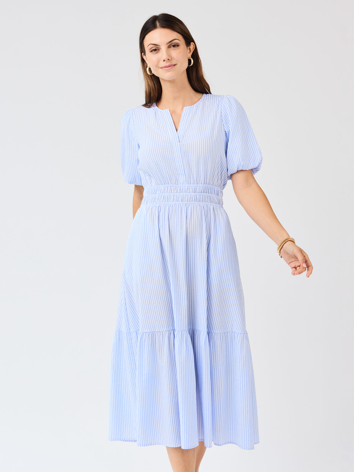 Woman wearing a light blue seersucker midi dress with puff sleeves a white background