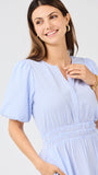 Woman wearing a light blue seersucker midi dress with puff sleeves a white background