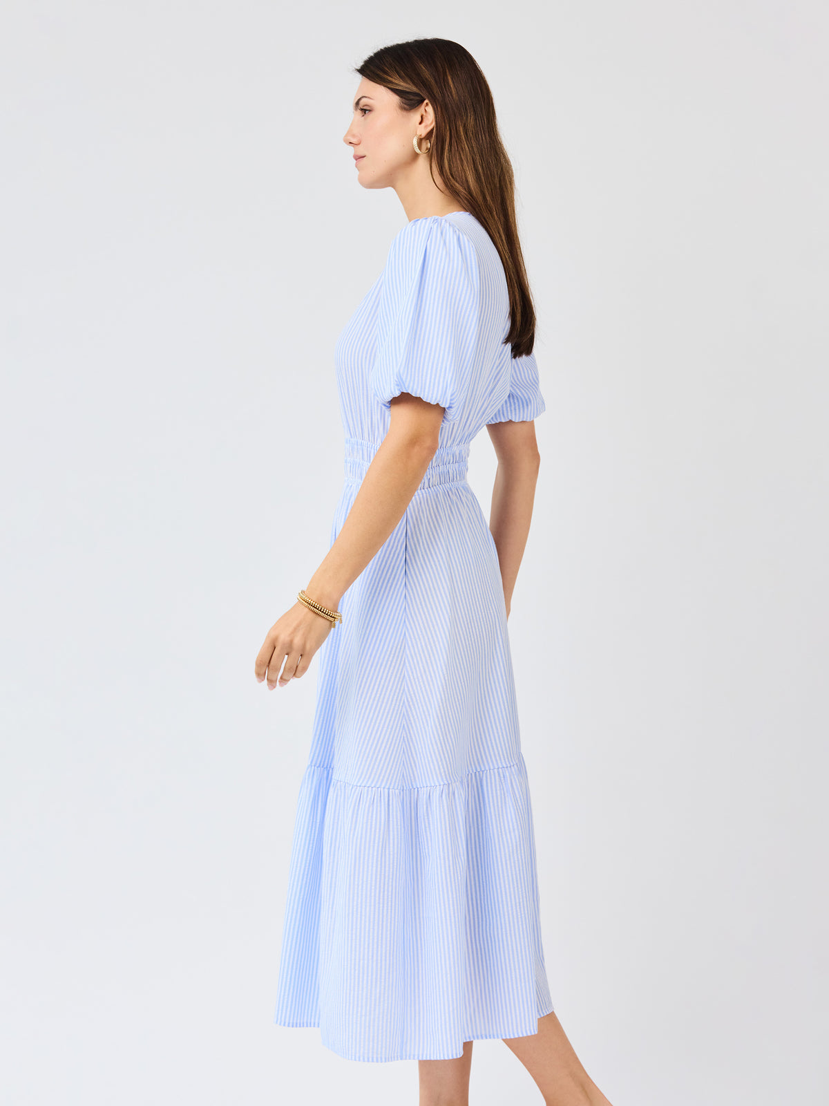Woman wearing a light blue seersucker midi dress with puff sleeves a white background