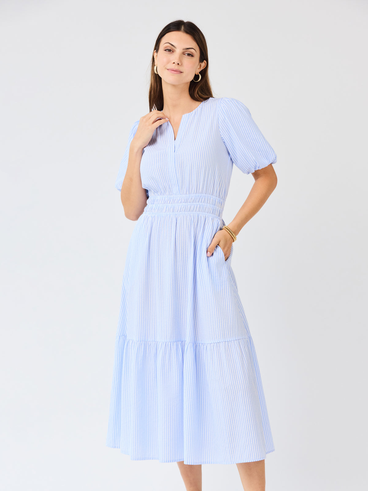 Woman wearing a light blue seersucker midi dress with puff sleeves a white background