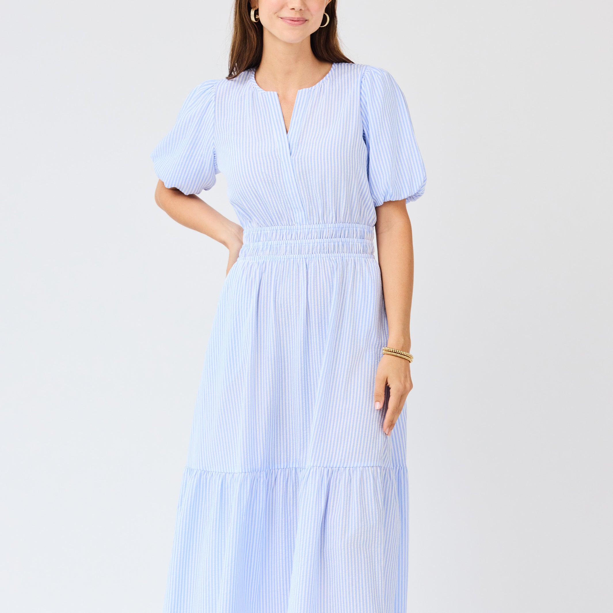 Woman wearing a light blue seersucker midi dress with puff sleeves a white background
