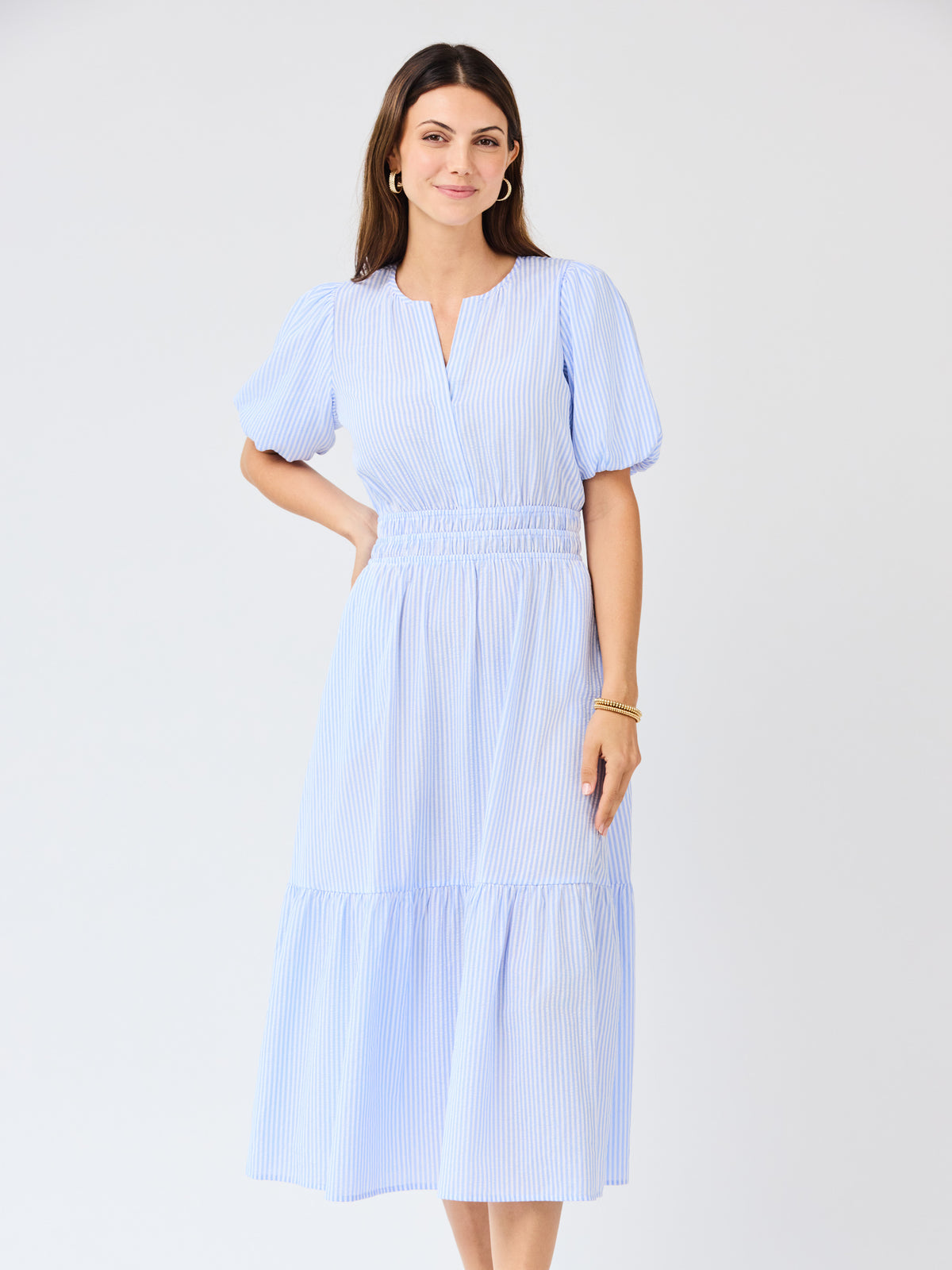 Woman wearing a light blue seersucker midi dress with puff sleeves a white background
