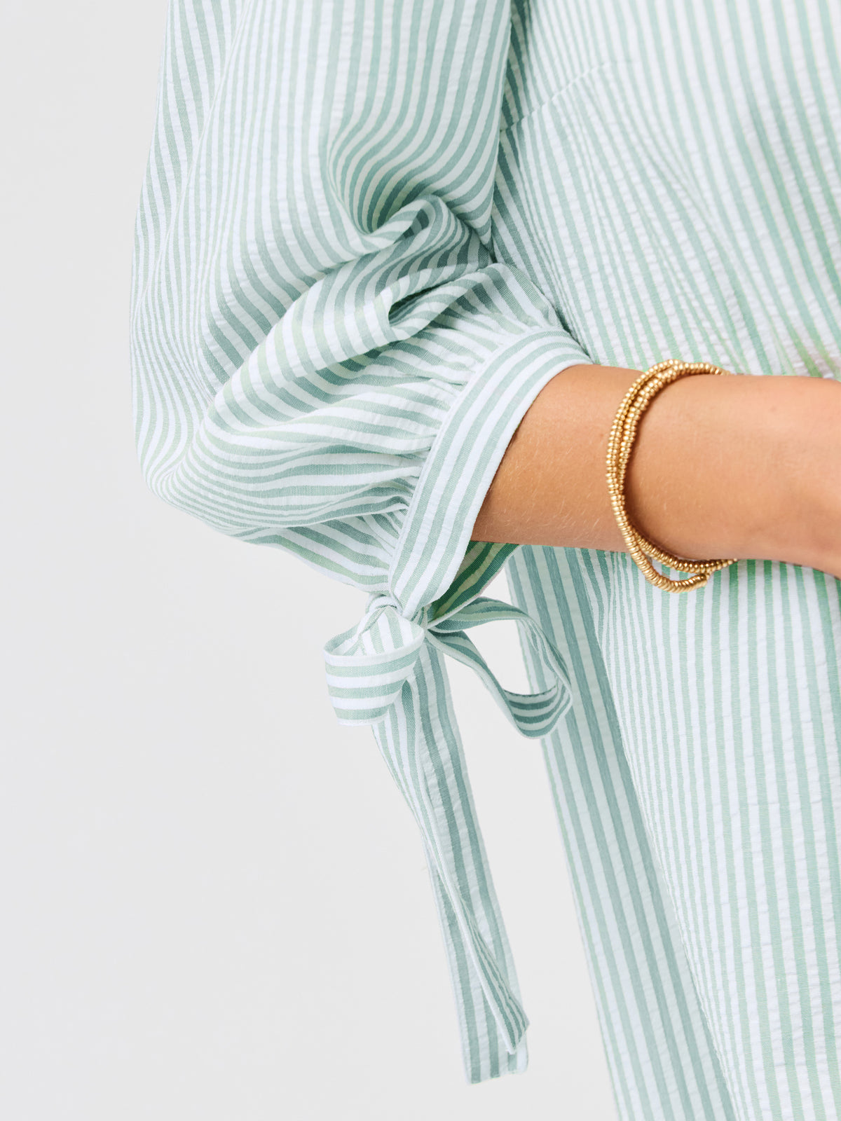 Green and white striped shirt with a tie detail on a light gray background