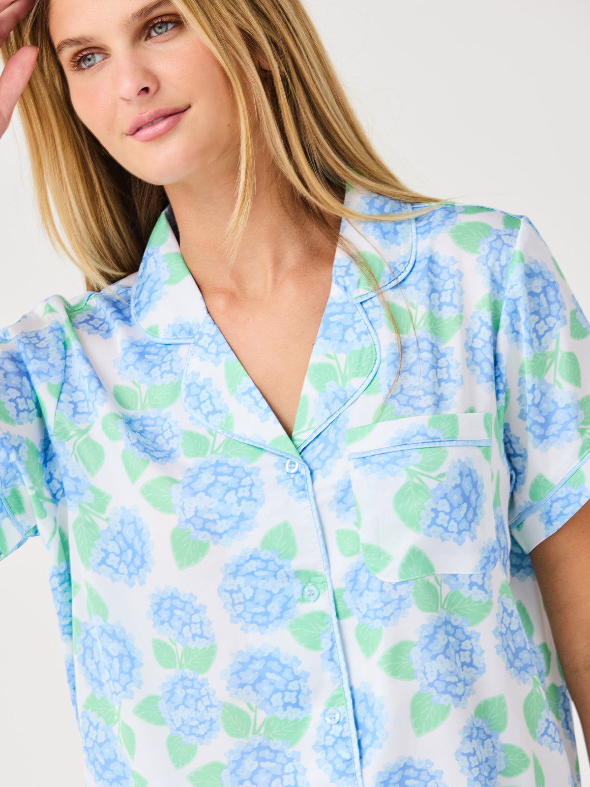 Woman wearing a floral patterned pajama set with blue and green flowers on a white background