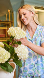 Woman in floral pajamas holding a bouquet of white hydrangeas indoors.