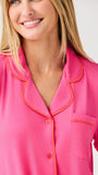 Woman wearing a pink pajama top with orange piping on a white background