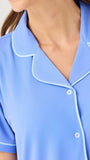 Close-up of a blue pajama top with white trim on a neutral background