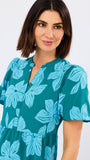 Woman wearing a teal dress with blue leaf patterns on a white background