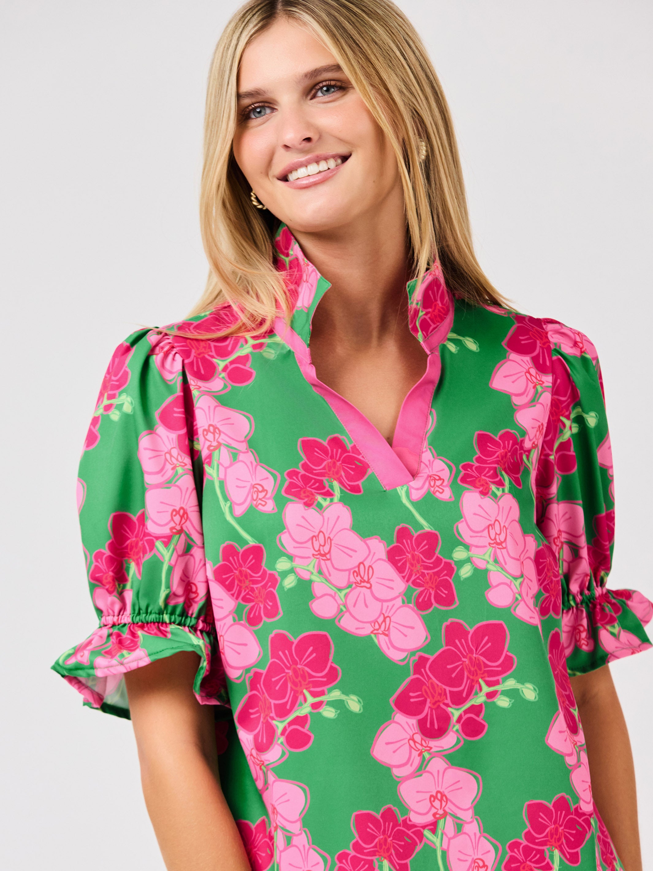 Woman wearing a green floral blouse with pink flowers on a white 