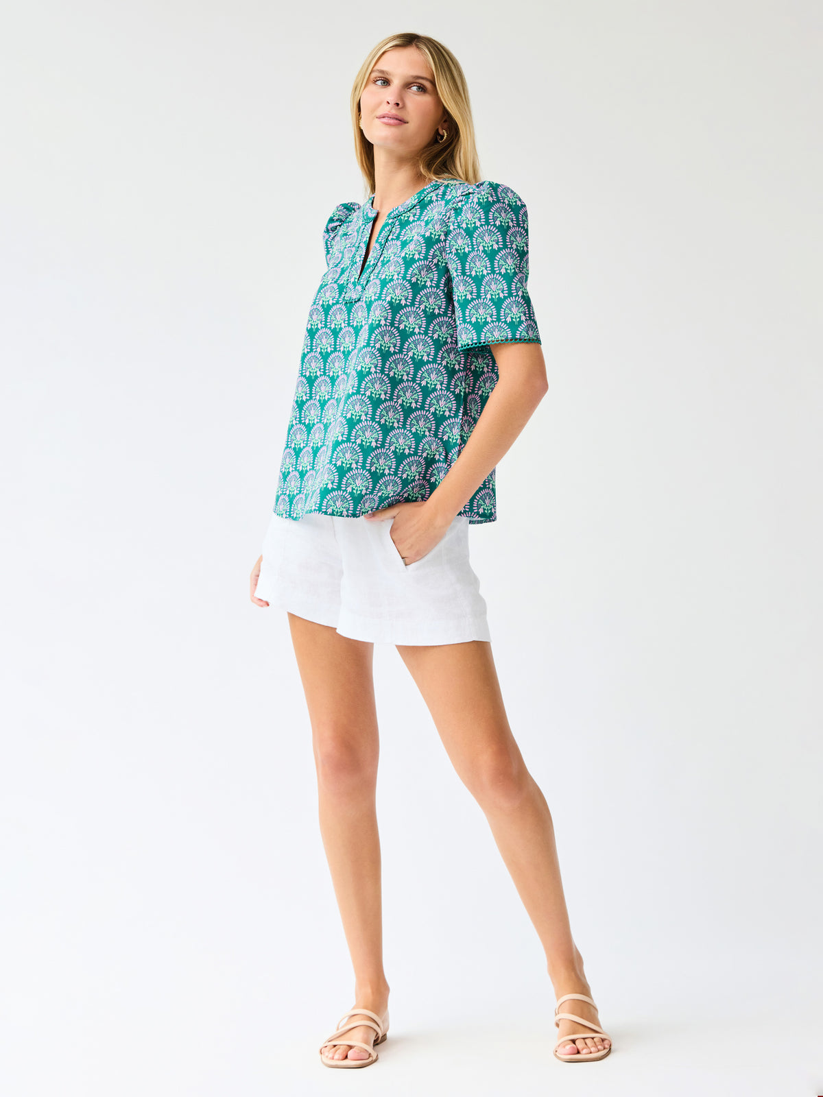 Woman wearing a teal patterned top and white shorts on a light gray background