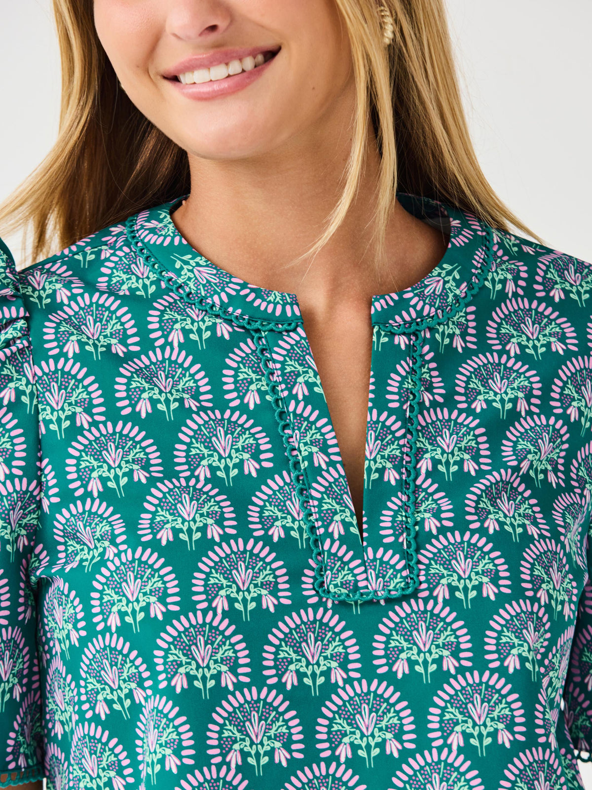 Woman wearing a teal patterned top and white shorts on a light gray background