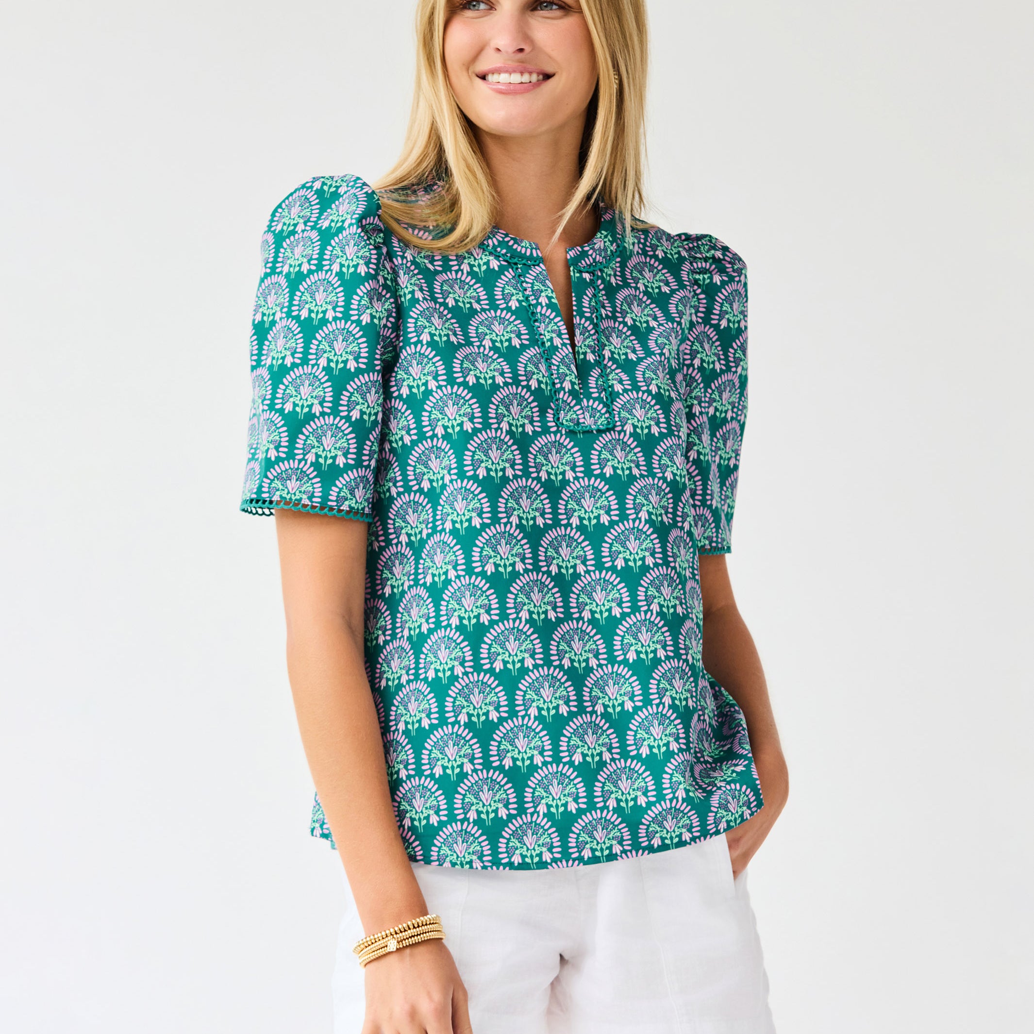 Woman wearing a teal patterned top and white shorts on a light gray background