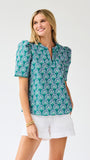 Woman wearing a teal patterned top and white shorts on a light gray background