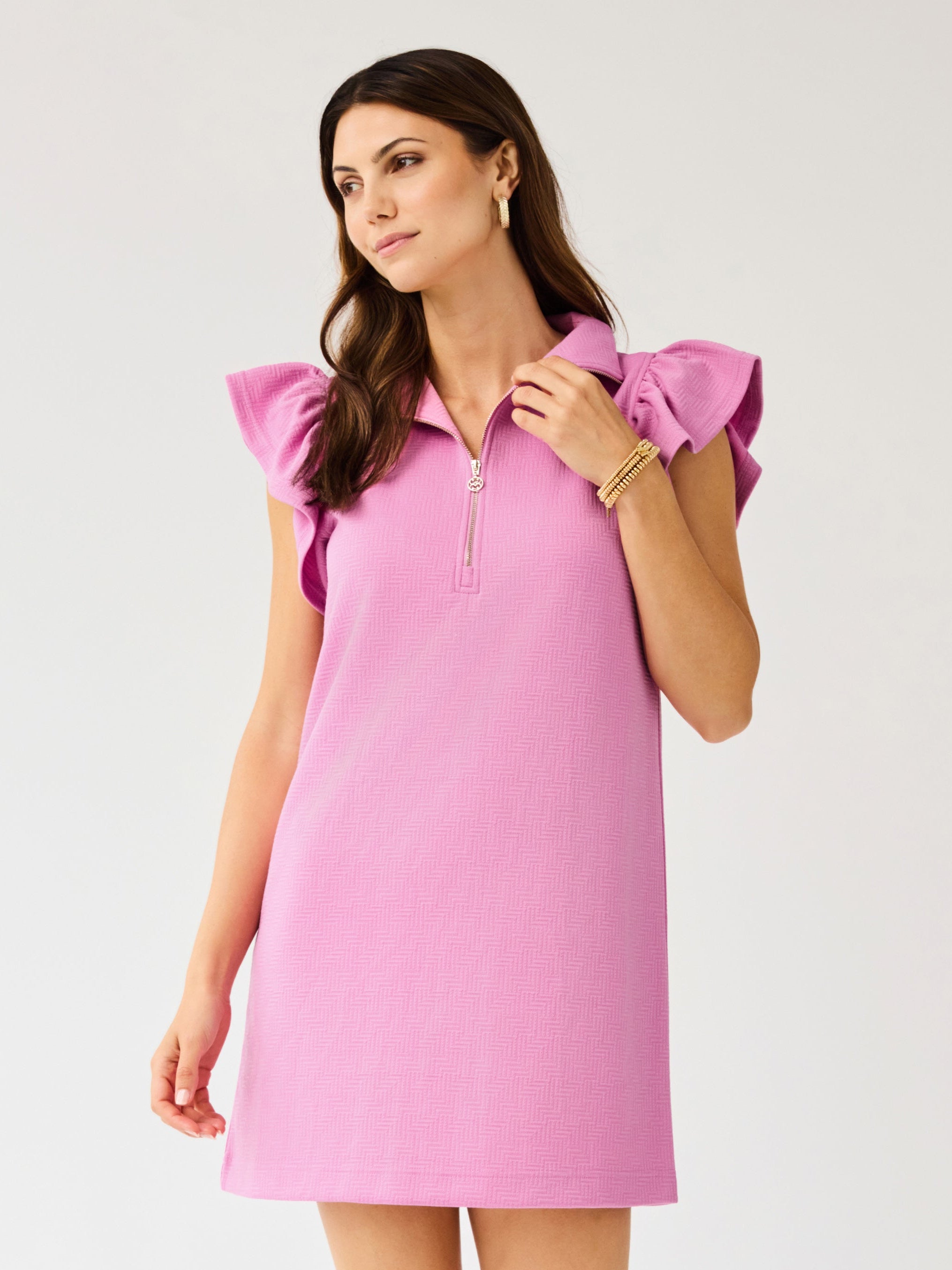 Woman wearing a pink dress with ruffled sleeves on a light gray background
